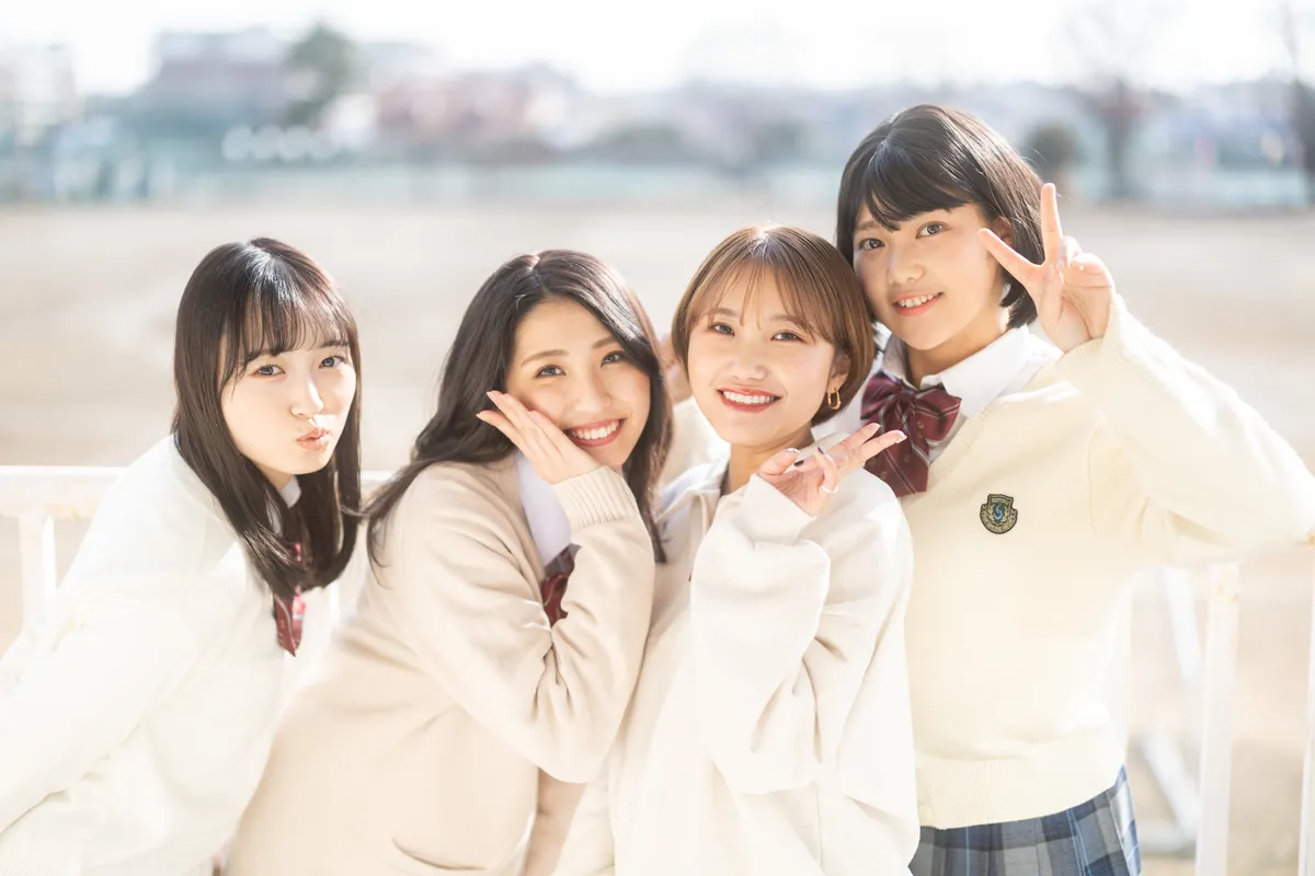 制服姿の4人が校庭で笑顔を見せる撮影カット